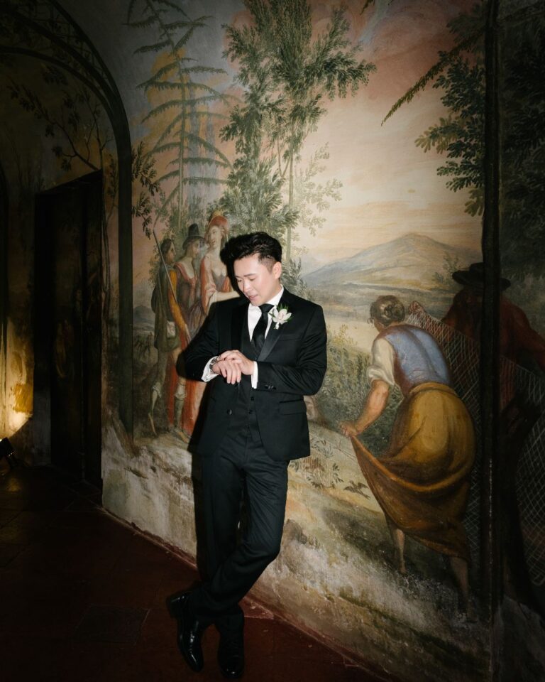 The groom in a classic black tuxedo, adjusting his bowtie before the ceremony.