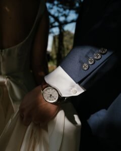 A close-up detail of the groom’s hand resting on a table, wearing a classic watch that adds a refined touch to his wedding look.