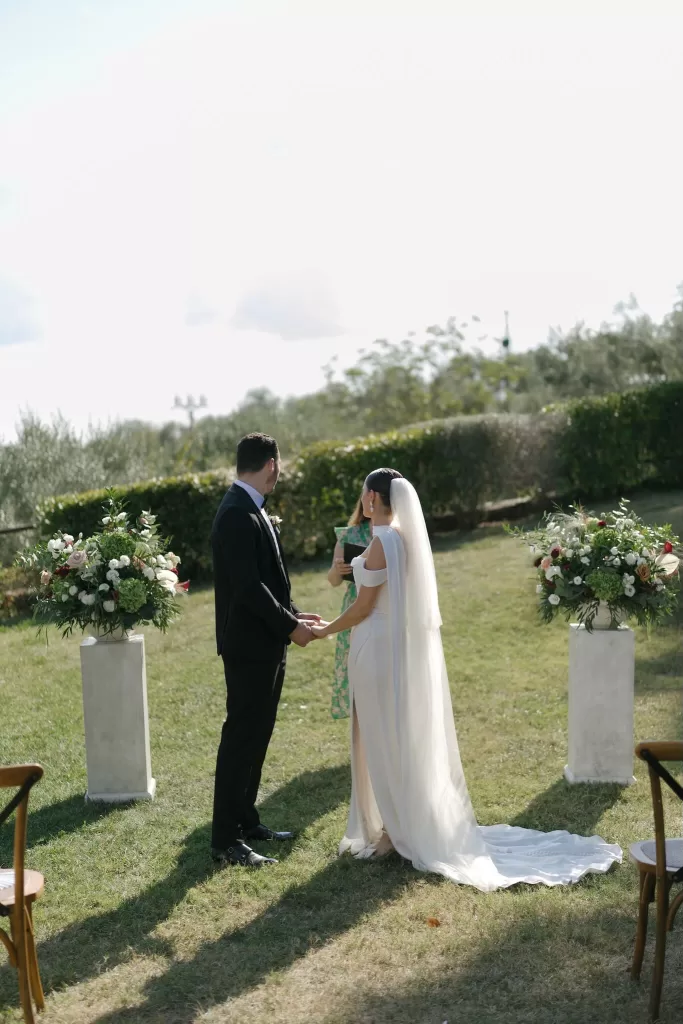Bride and groom holding hands during their outdoor ceremony surrounded by floral pillars at Quercia al Poggio.