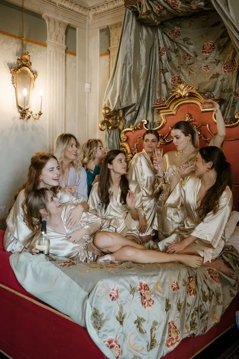 Bridesmaids relaxing with champagne on a floral bedspread at Borgo Stomennano