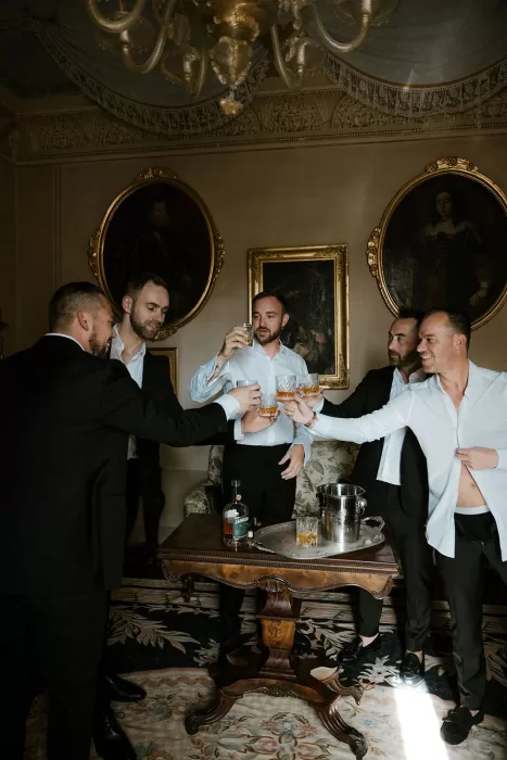 Groomsmen toasting with whiskey in an opulent room at Borgo Stomennano