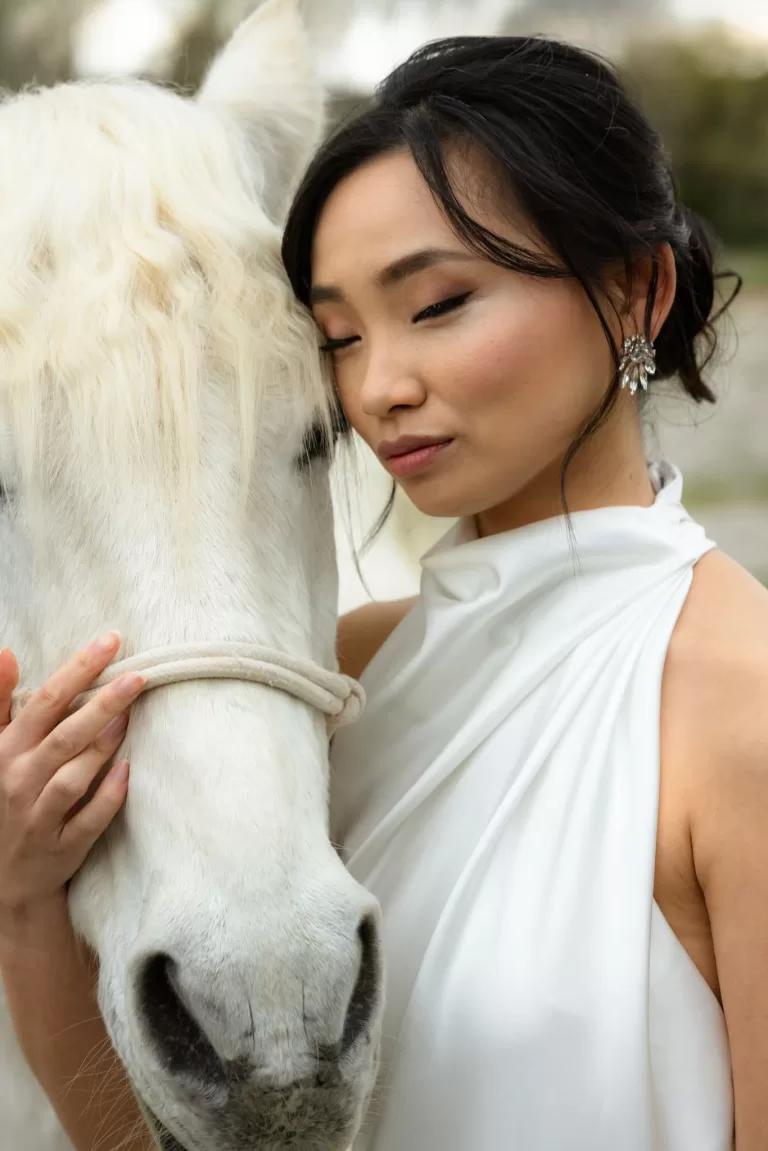 Intimate bridal portrait with the bride resting her face against a white horse, captured in soft natural light by Lima de Miguel.