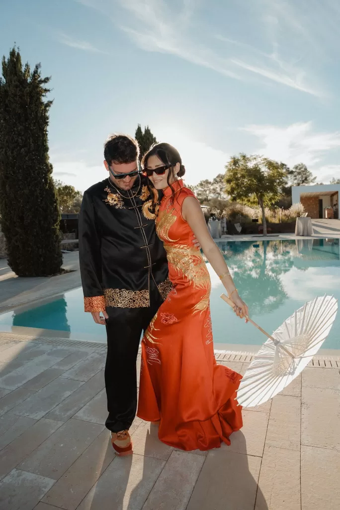 Bride and groom pose stylishly by the pool at Ca Na Xica, bride holding a white parasol in the sunshine.
