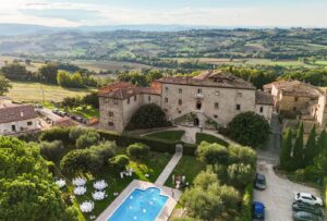 Aerial view of Castello Montignano and its lush Umbrian surroundings, showing the pool, gardens, and medieval stone architecture.