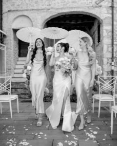 Bride and bridesmaids laughing and walking with paper parasols after the ceremony at Castello Montignano.