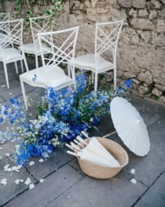 White ceremony chairs with blue delphinium arrangements and parasols at Castello Montignano wedding.