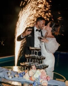 Bride and groom share a kiss during a champagne tower toast with fireworks in the background at Castello Montignano.