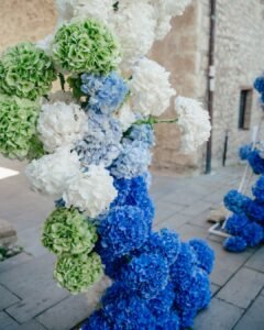 Close-up of vibrant blue, green, and white hydrangea floral arch in the stone courtyard of Castello Montignano.