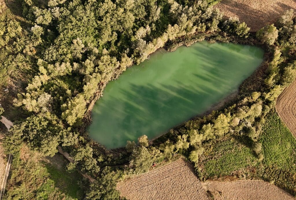 Serene aerial view of a green lake near Castello Montignano, nestled within the rolling Umbrian countryside.