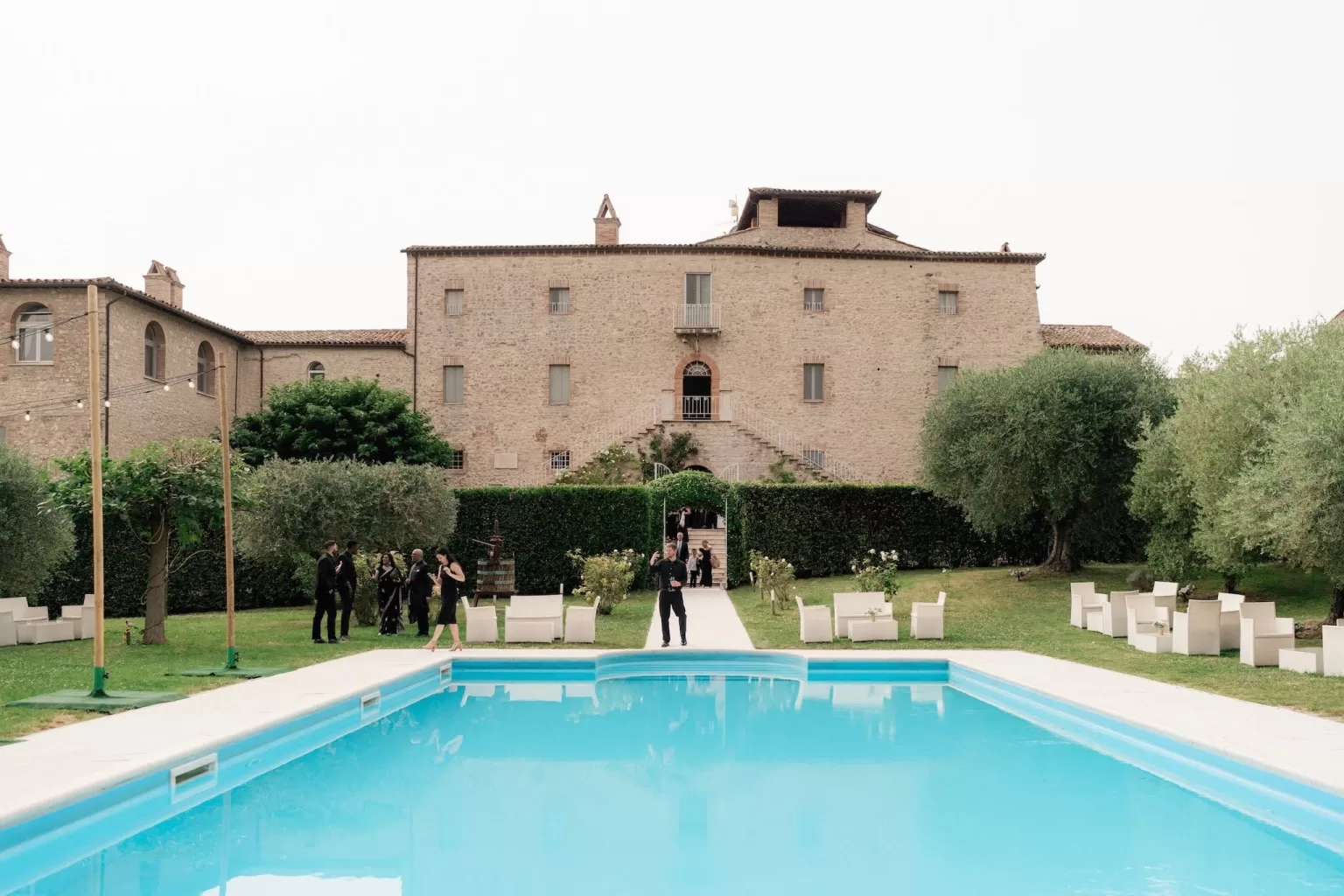 Guests mingling by the pool in front of Castello di Montignano’s historic stone façade