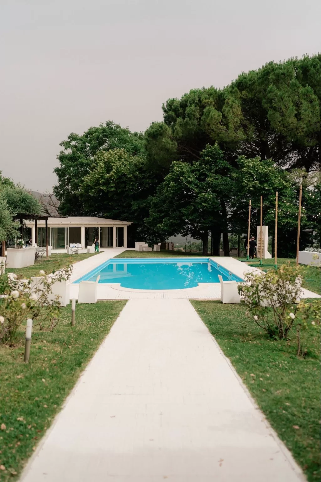 Elegant garden pool area at Castello di Montignano, surrounded by trees and white lounge furniture.
