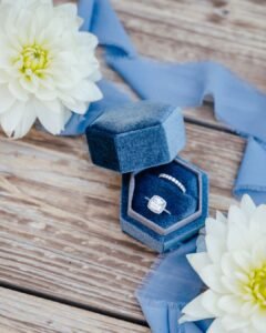 Engagement ring and wedding band in a velvet box with white dahlias and silk ribbon on rustic wood at Castello Montignano.