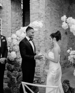 Bride and groom exchanging vows at Castello Montignano, surrounded by romantic floral arches and historic stone walls.