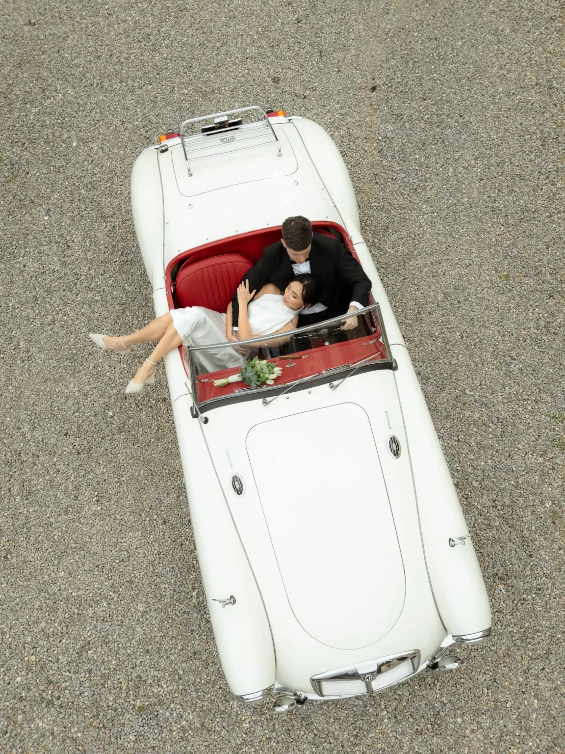 Overhead shot of a newlywed couple reclining in a vintage car, styled with fashion-led elegance by Lima de Miguel.