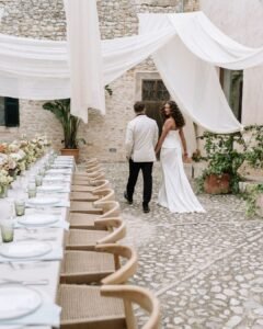 Bride and groom walking hand-in-hand in the charming stone courtyard of Finca Morneta, featuring beautifully styled reception tables.