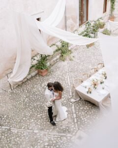 Romantic overhead perspective capturing newlyweds embracing in the idyllic courtyard of Finca Morneta, styled with delicate drapery and florals.