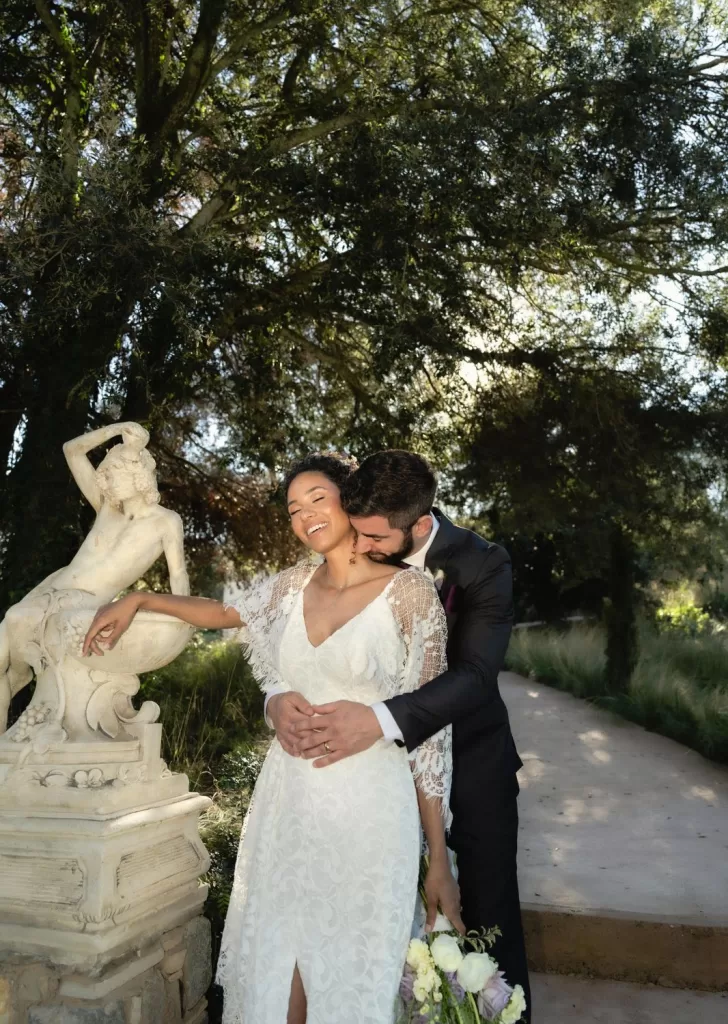 Joyful moment between bride and groom captured by a sculpture in Mas Torroella’s sunlit garden.