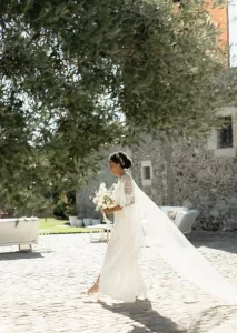Bride walking gracefully across the cobbled courtyard at Mas Torroella with her bouquet and veil flowing behind.
