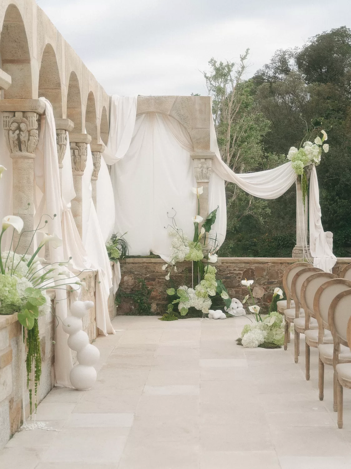 Wide view of floral-filled wedding ceremony framed by ancient arches at Mas Torroella.