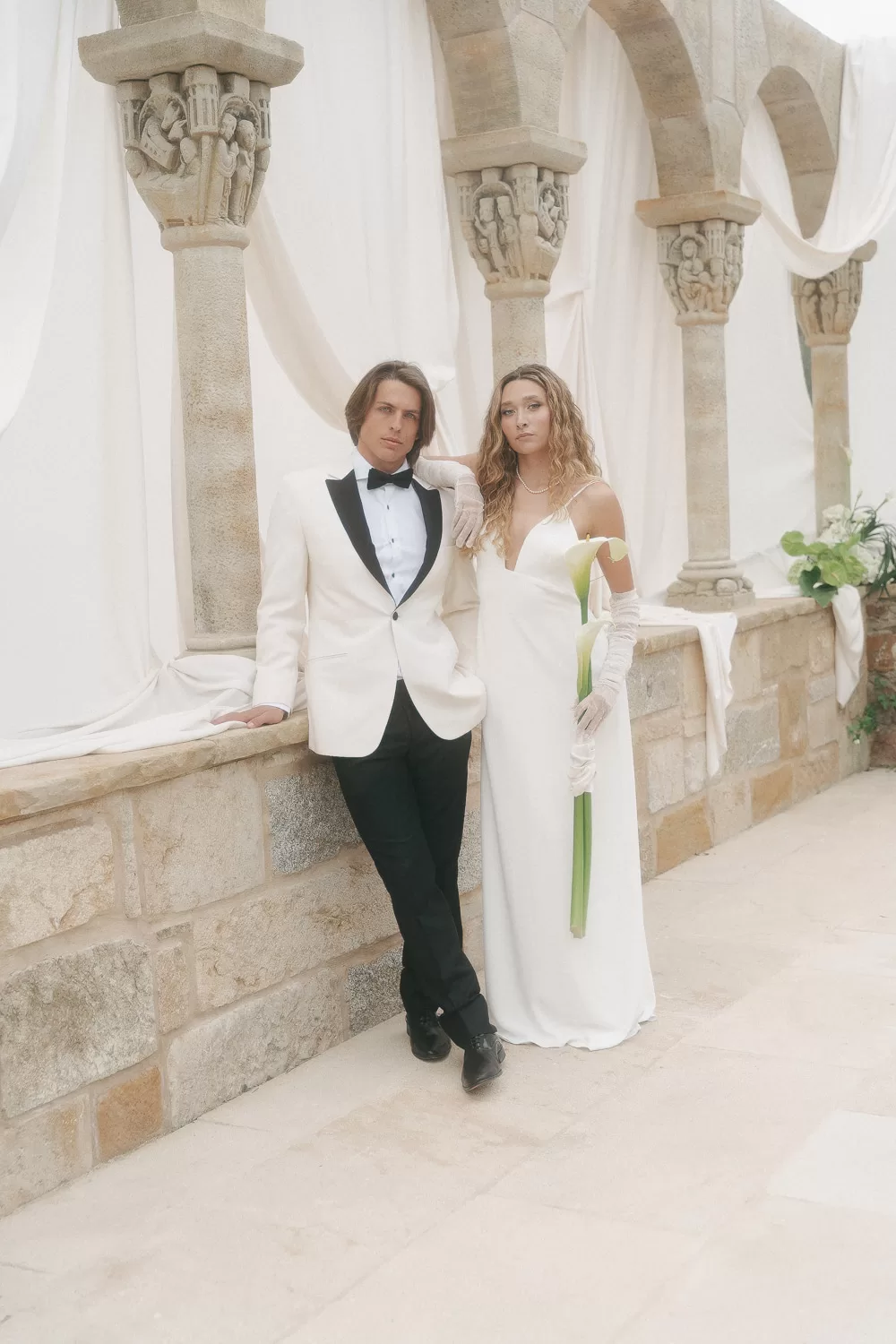 Fashion-forward couple standing confidently beneath ivory-draped arches at Mas Torroella.