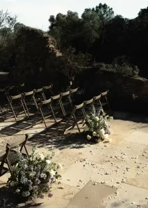 Soft purple and white flower arrangements line the aisle at Mas Torroella, surrounded by natural stone and forest.