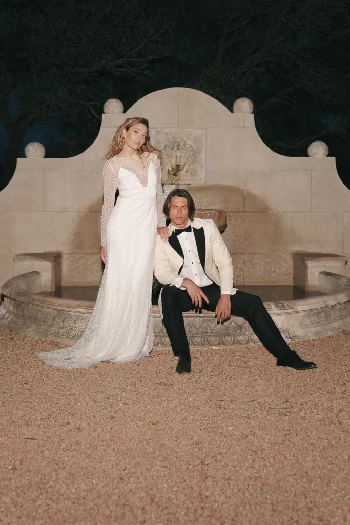 Elegant wedding portrait by the stone fountain at night at Mas Torroella with the bride in a long-sleeved gown.