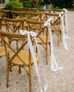 Close-up of wooden chairs with long white ribbons lining the aisle for an outdoor wedding ceremony at Château Rigaud.