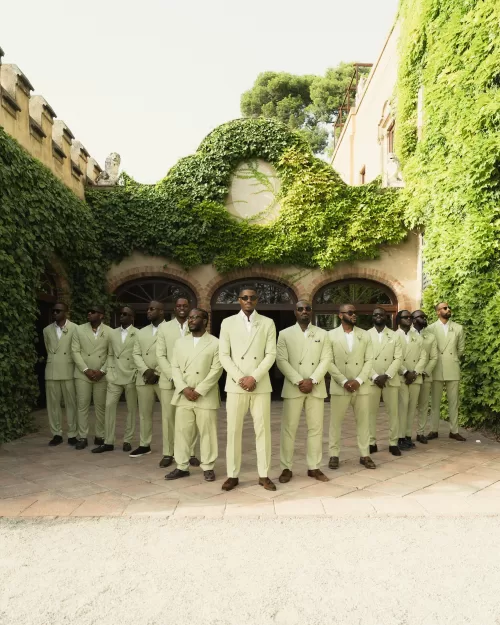 Groomsmen standing in formation against ivy-covered walls in light green suits, exuding elegance and unity in Ruben Larruy’s photo.