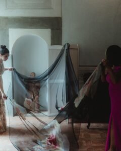 Bridesmaids preparing a floral-embroidered black veil beside a niche statue in Villa Ivana’s classic setting.