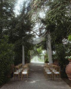 Romantic outdoor aisle at Villa Ivana lined with gold chairs and draped white fabric beneath towering cedar trees.
