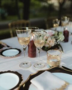 Elegant gold-rimmed glassware set on a white linen table for the wedding reception at Villa Ivana.