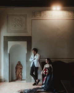 Bride and groom captured in moody window light at Villa Ivana, standing near a terracotta statue and vintage furniture.