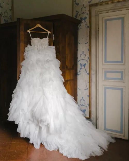 The wedding dress hangs elegantly in a sunlit room, awaiting the bride’s final touches.