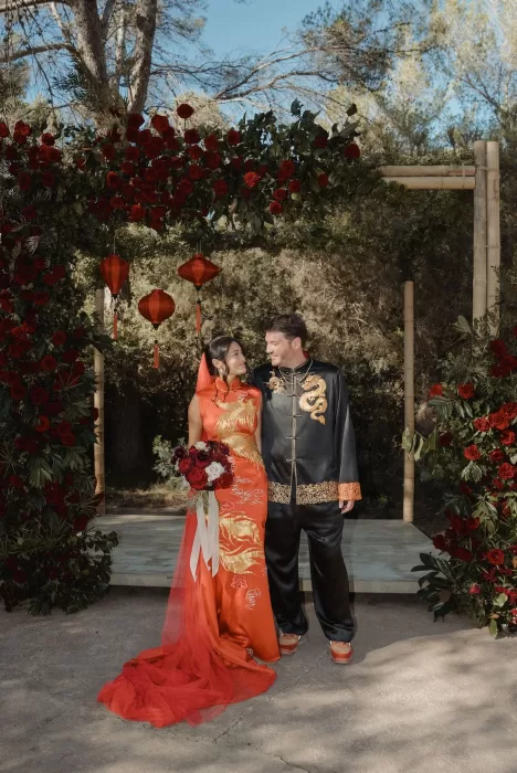 Couple standing beneath a floral arch with red lanterns at Ca Na Xica, surrounded by forest greenery.
