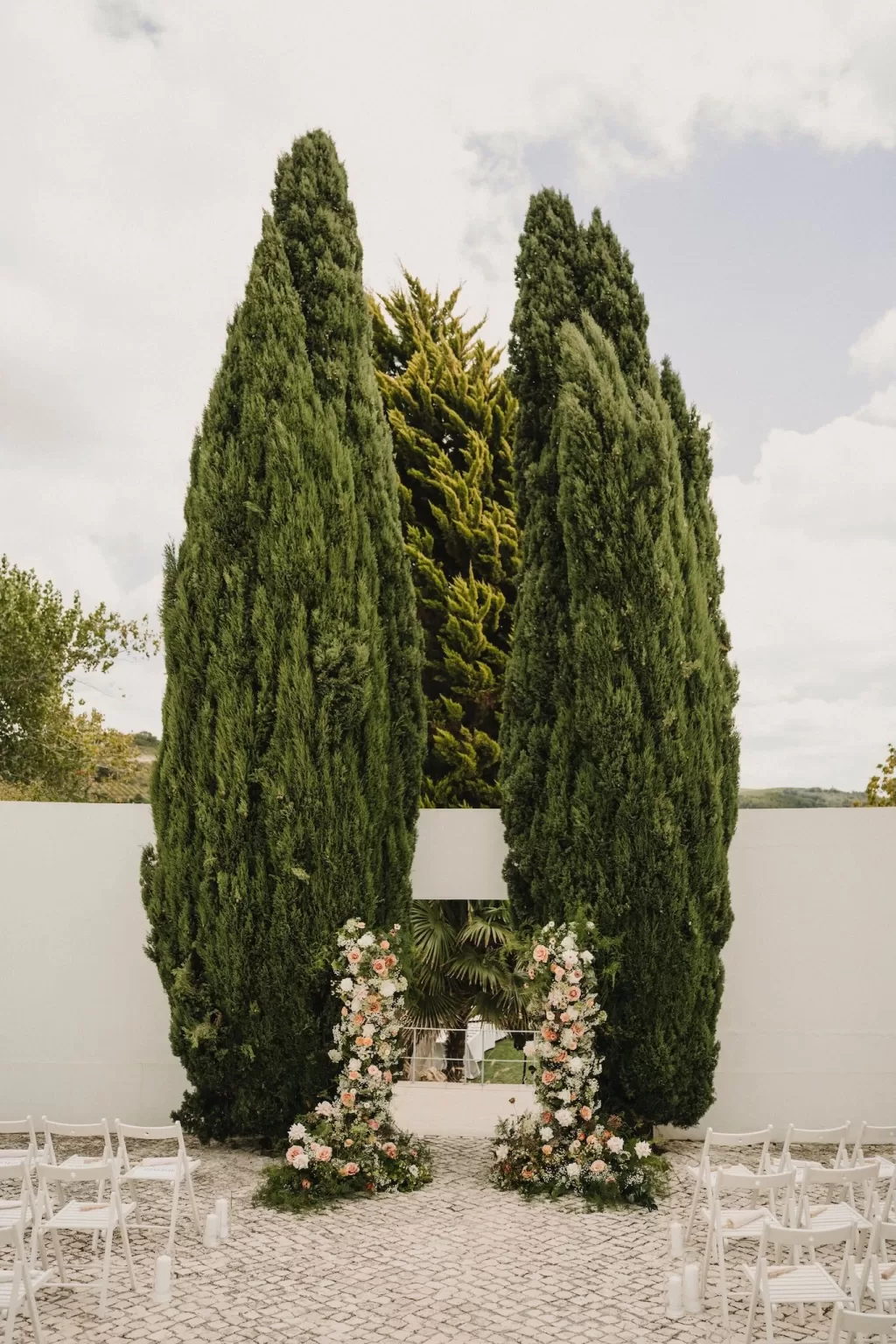 Wedding ceremony under the trees at Casa Sacoto with a floral arch and wooden chairs.