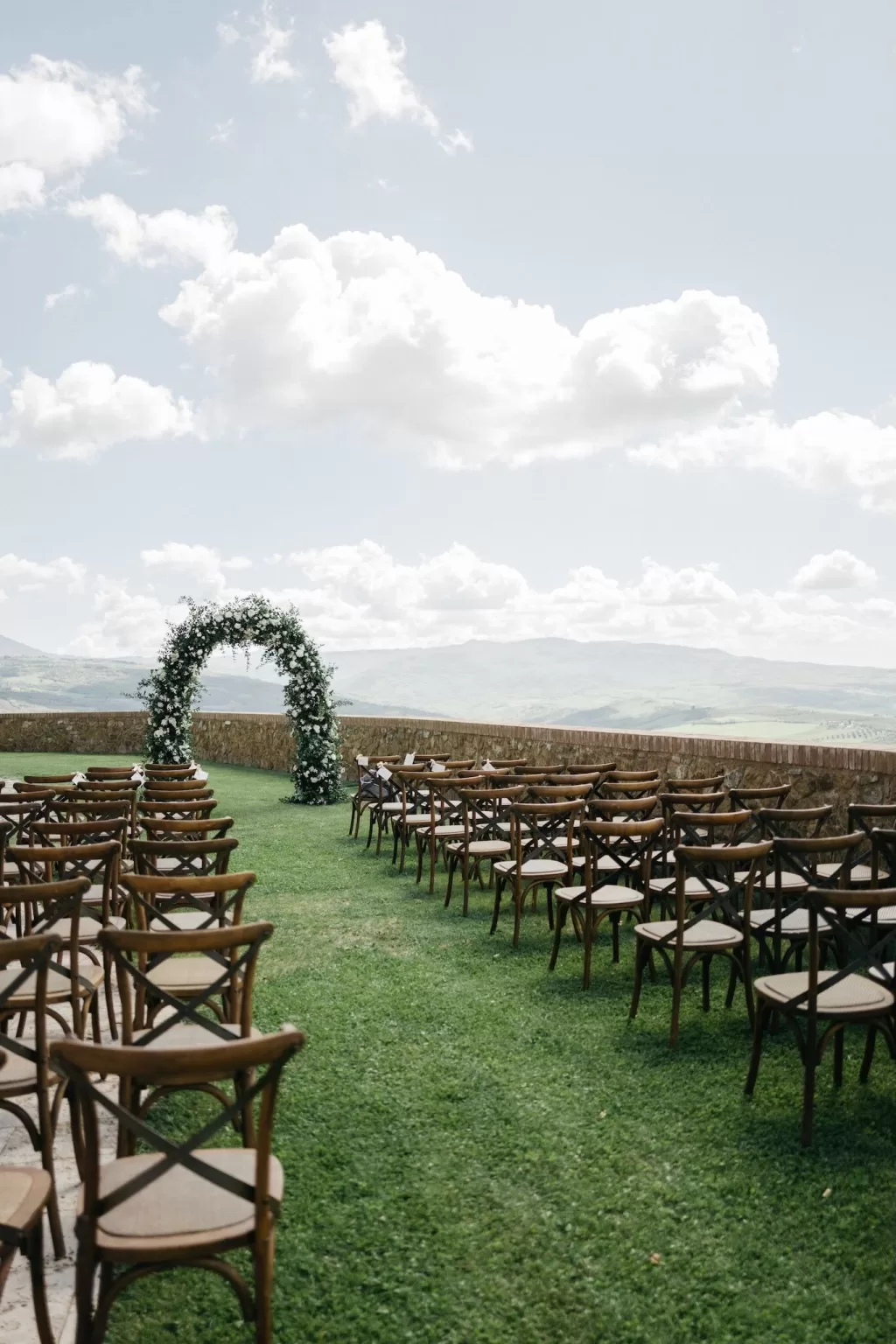 Outdoor wedding ceremony setup with wooden chairs and floral arch overlooking Tuscan hills at Castello di Velona.