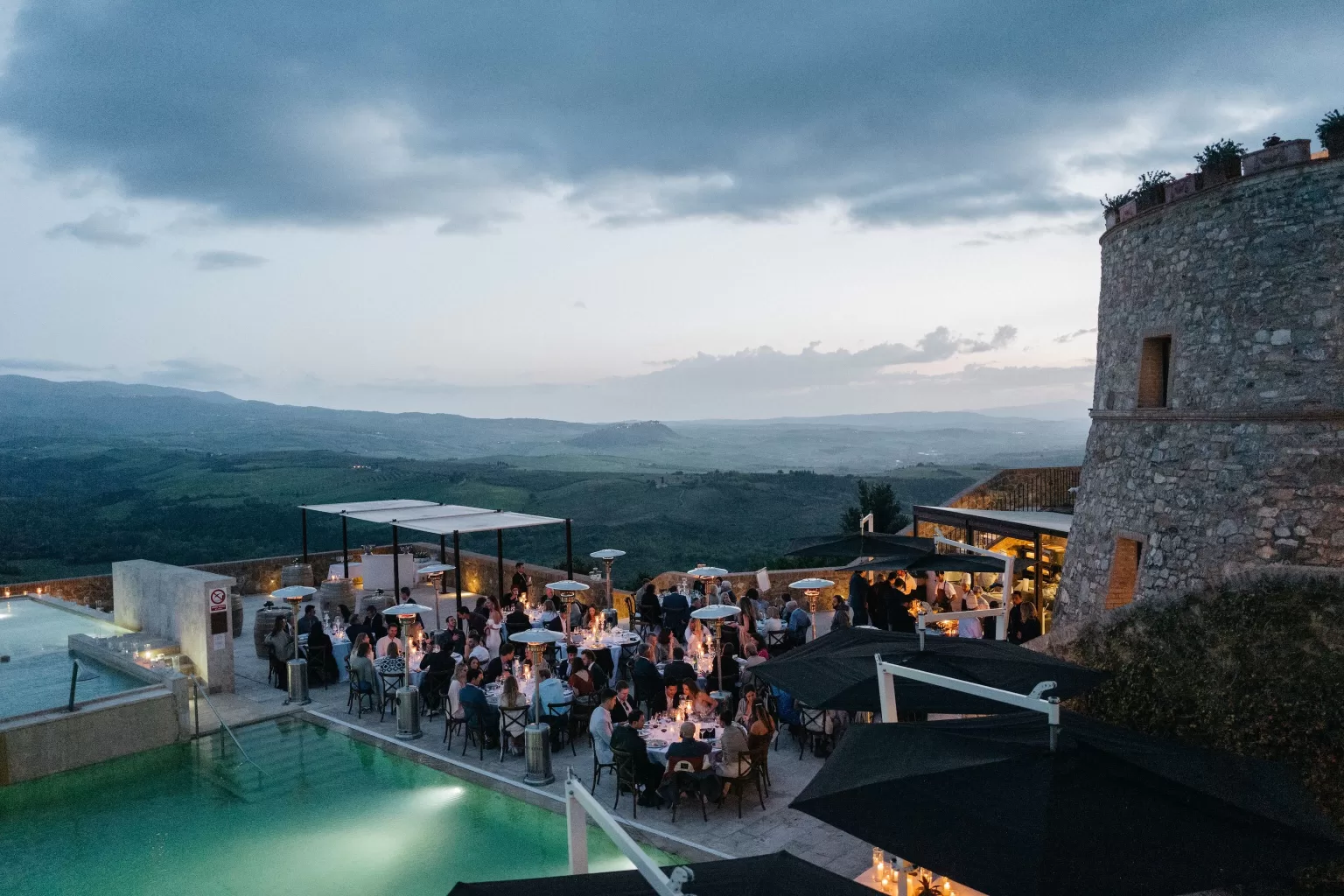 Wedding reception dinner by the illuminated pools at Castello di Velona at dusk.