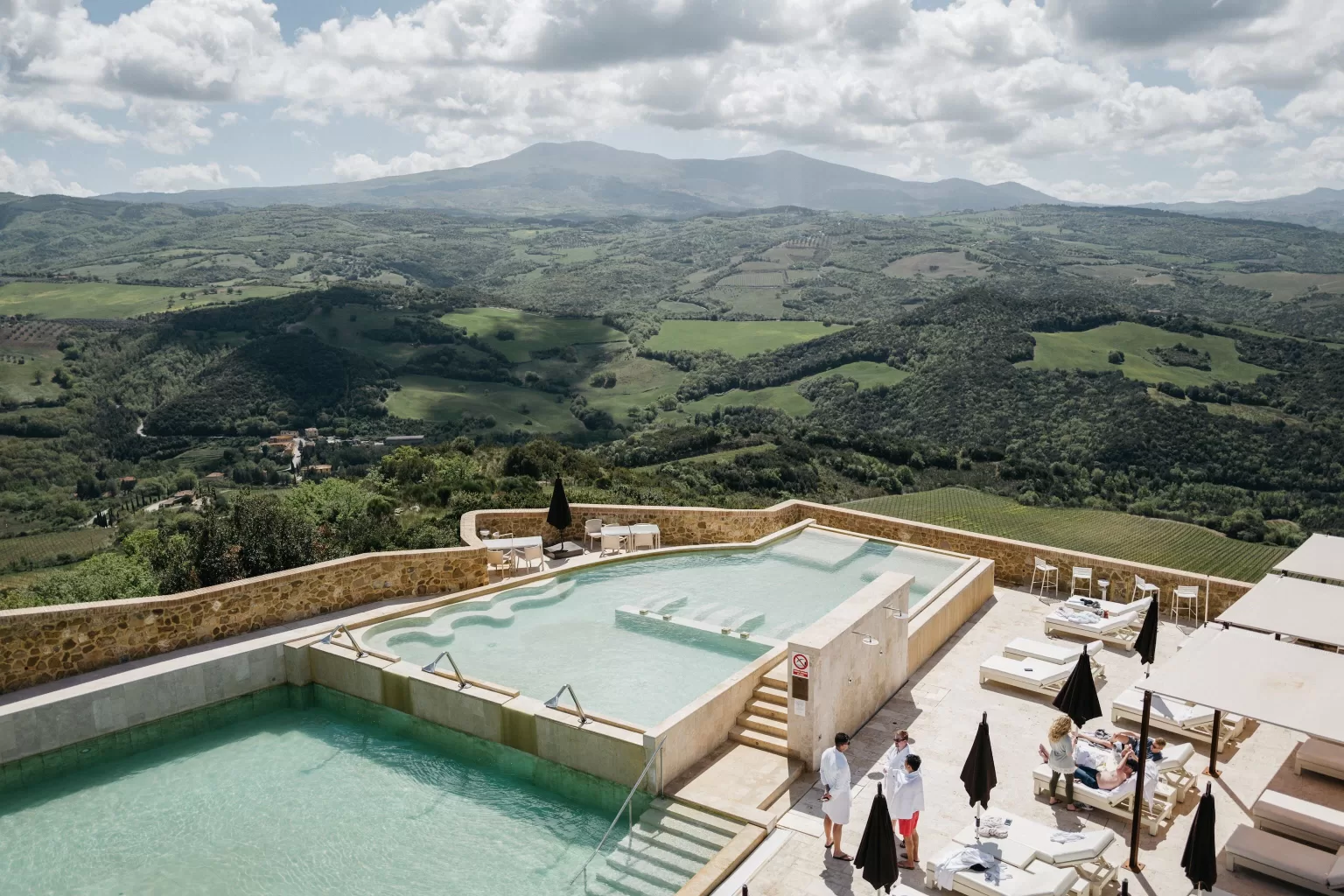 Illuminated infinity pools at Castello di Velona with panoramic Tuscan valley views at dusk.