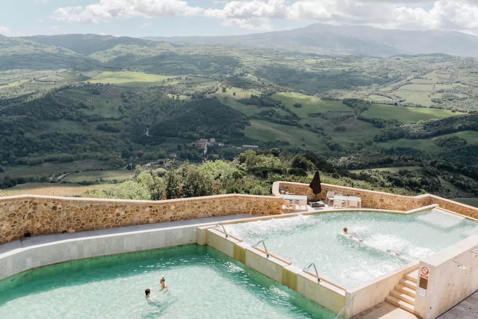 Panoramic view of the thermal pools at Castello di Velona surrounded by Tuscan hills.