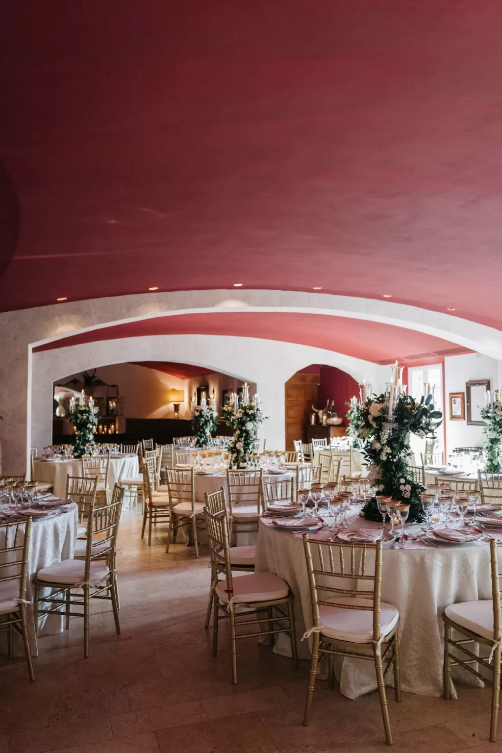 Elegant wedding reception hall at Castello di Velona with round tables, gold chairs, and tall floral arrangements.