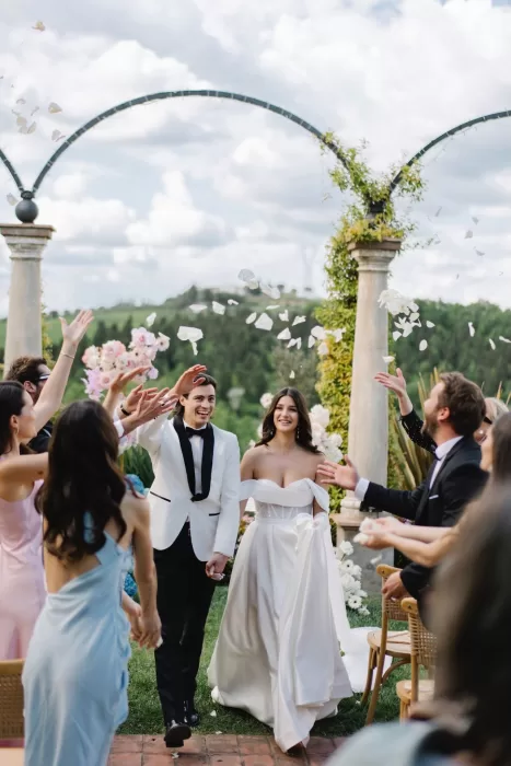 The newlyweds celebrating their ceremony exit under falling petals at Tenuta Corbinaia, surrounded by friends and scenic Tuscan hills.