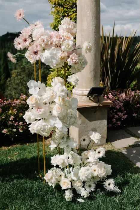 Elegant blush and white floral arrangements decorating the ceremony space at Tenuta Corbinaia, set against lush greenery.