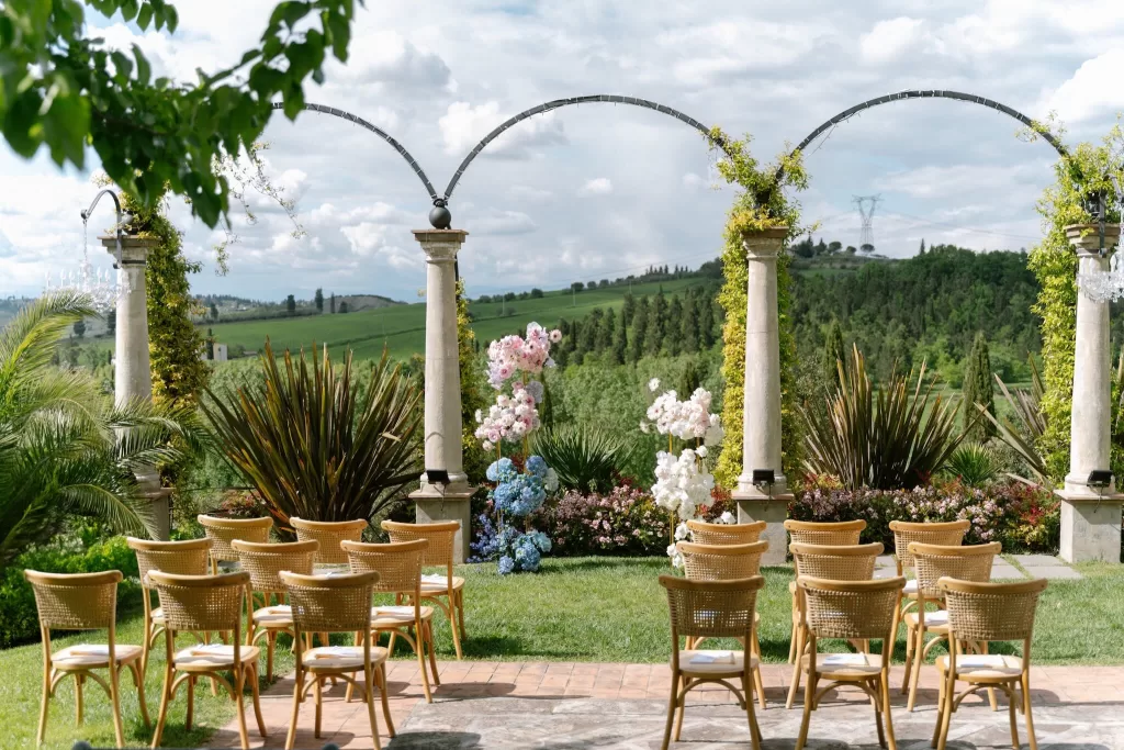 Outdoor ceremony setup at Tenuta Corbinaia featuring wooden chairs and floral pillars overlooking the Tuscan countryside.
