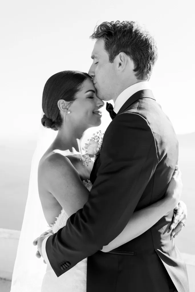 Bride and groom embrace on a sunlit terrace at Rocabella Santorini, overlooking the Aegean Sea