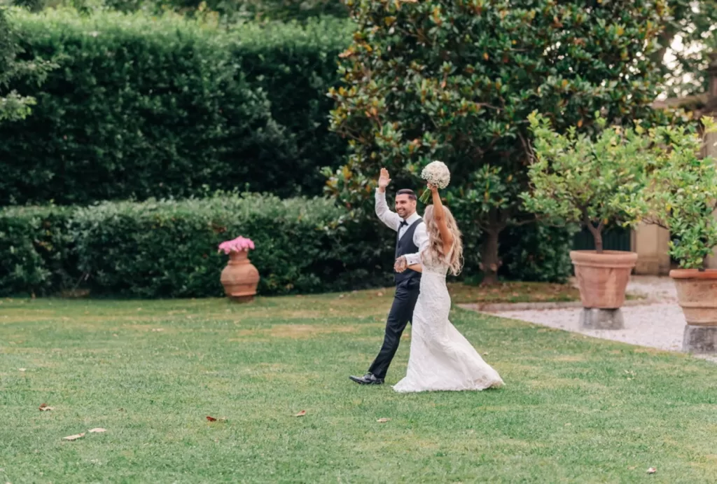 Bride and groom walking hand in hand through Villa Ravano’s lush Italian garden