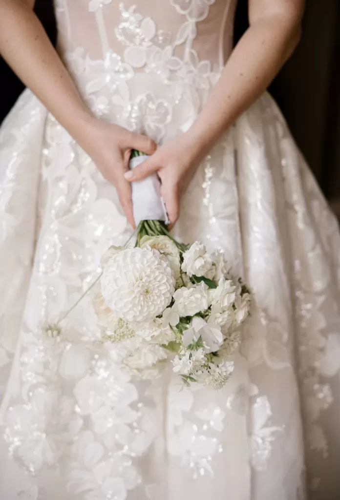Close-up of the bride’s hands holding a white floral bouquet, with delicate embroidery on her gown at Euridge Manor.