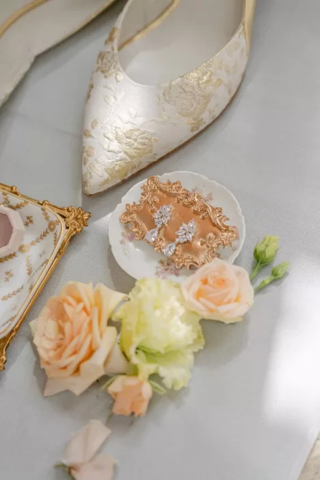 Flat lay of bridal accessories including floral heels, vintage earrings, and pastel blooms at Euridge Manor.
