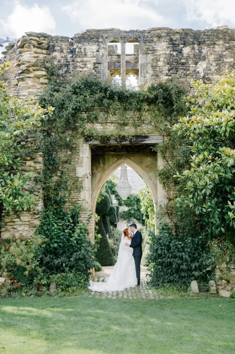 The couple shares a quiet kiss under a romantic stone arch covered in ivy at Euridge Manor.