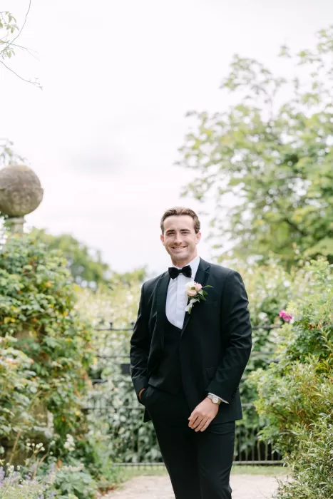 Groom in classic black tuxedo smiling in the lush garden surroundings of Euridge Manor.