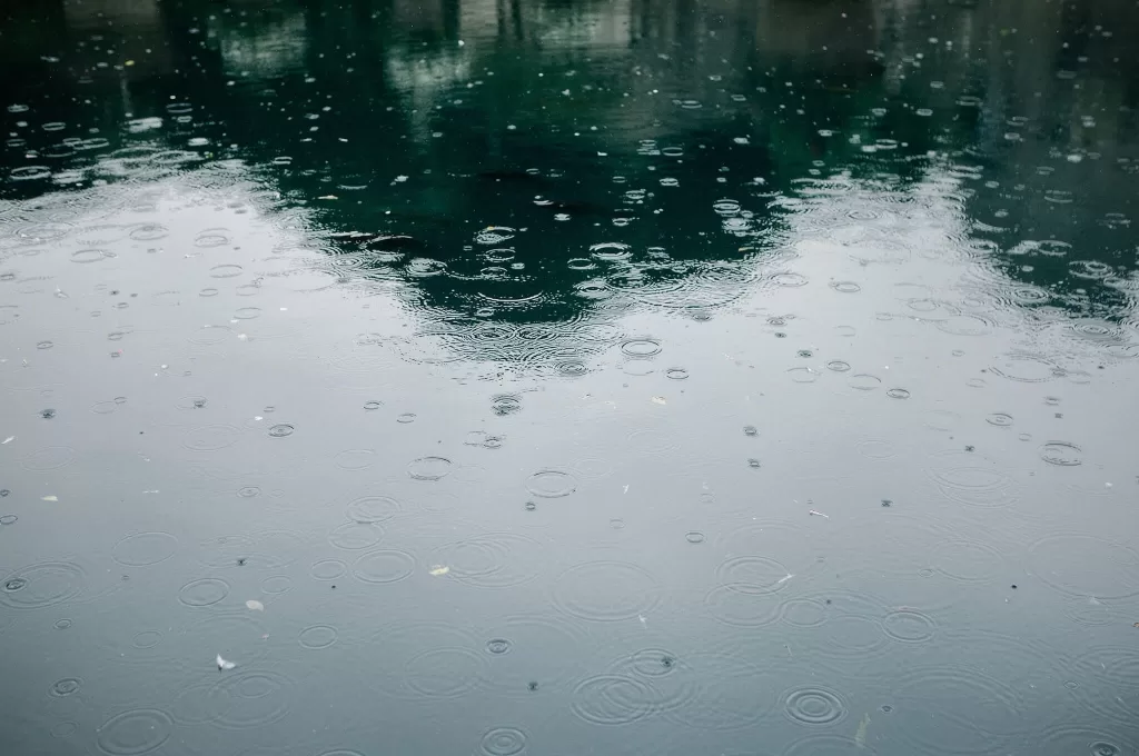 Raindrops create ripples across the water at Euridge Manor, with the venue's silhouette reflected on the surface.